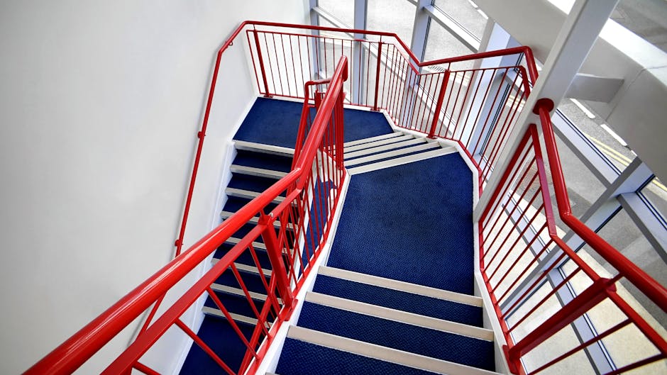 The image depicts a wooden staircase in a residential interior, with beige-painted steps and a dark burgundy carpet runner extending along the center. Natural light streams in through a large, multi-p