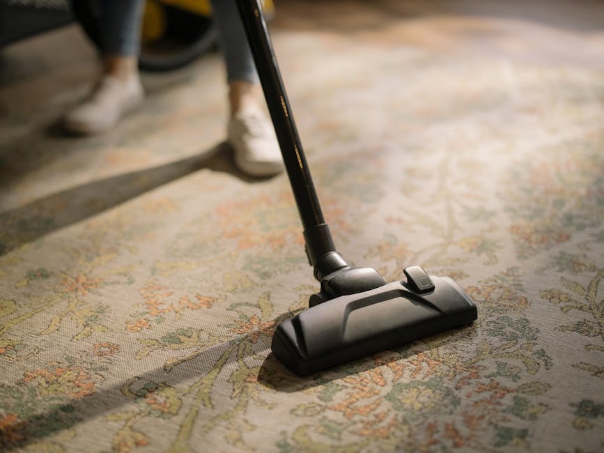 Two technicians from Kennington Carpet Cleaners are performing surface cleaning and sanitisation on a black car inside a well-lit garage. The technician on the left, wearing a black T-shirt with the c
